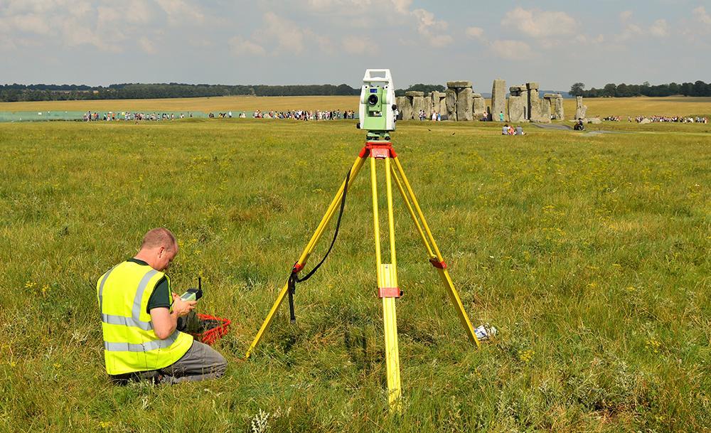 A scientist with surveying equipment looking at Stonehenge in the distance