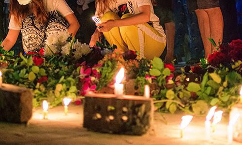 People surrounding candles and flowers at a vigil