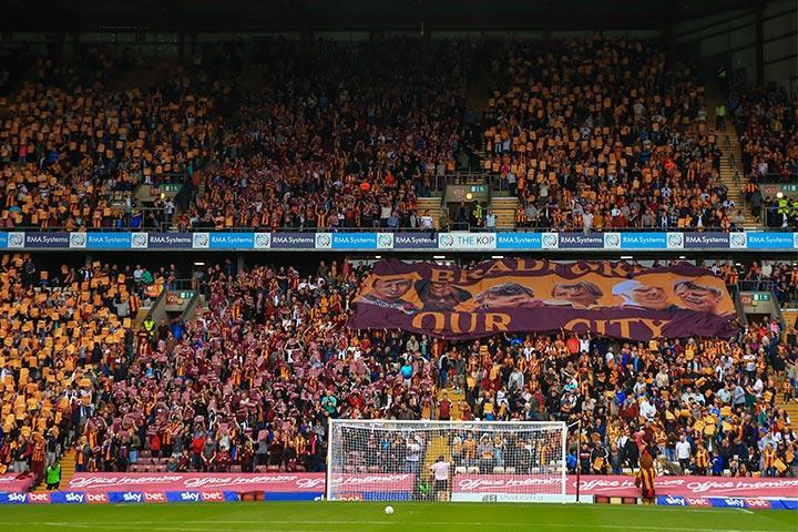 Bradford City AFC Stadium with people sat in the stands, spectating a football game.