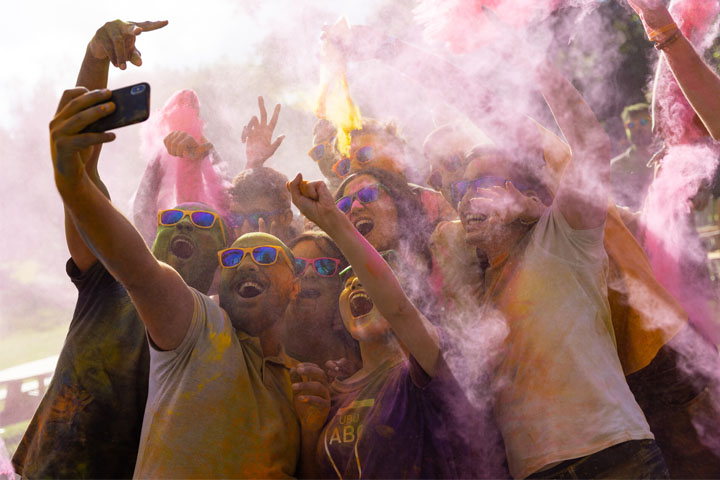 A group of students pose for a selfie while covered in colourful paint
