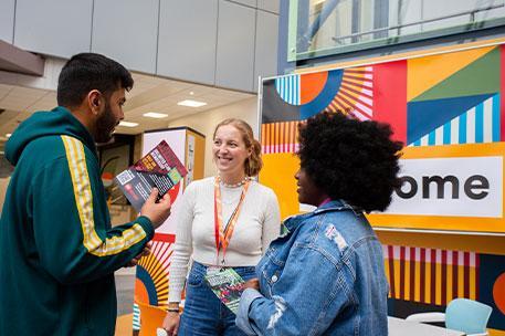 Three students chatting in front of a colourful welcome sign.