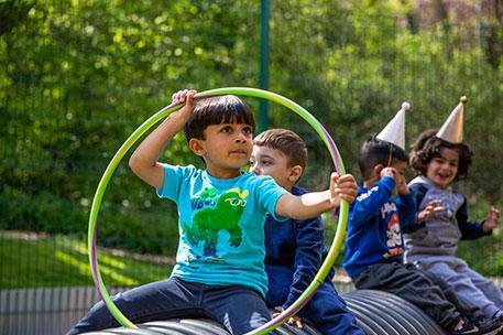 A child playing with a hoola hoop with other children in the background.