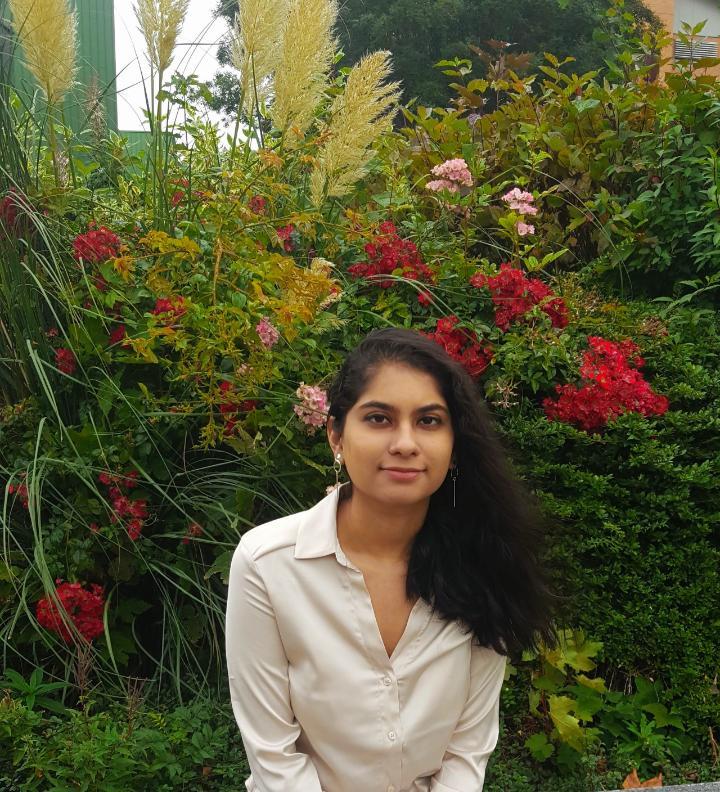 Sneha leaning forward in front of some greenery.