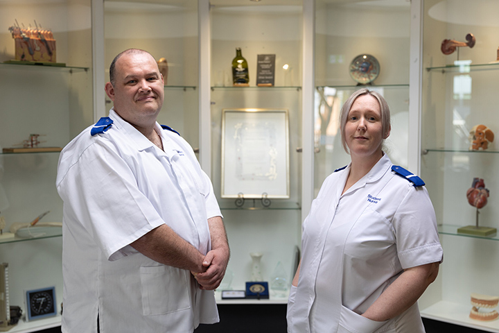Two adult learners stand in nursing uniform facing the camera and smiling