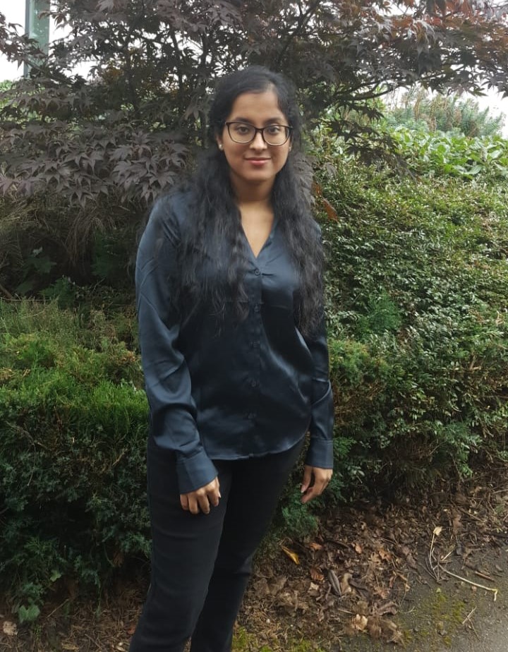 Sapna stood in front of a bush and trees.