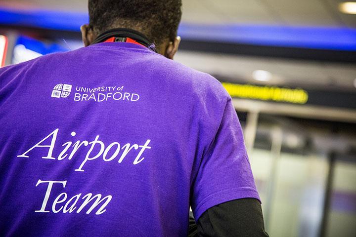 A member of the University airport team wearing a purple shirt with the University and Airport Team logos on the back