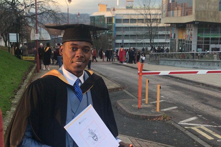 Billy Chabalenge in graduation attire with his certificate outside the Richmond building