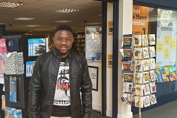 A student standing in the doorway of a bookshop, smiling at the camera.