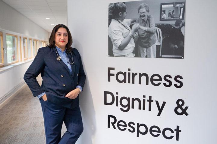A smartly dressed person standing next to some wall art with the words fairness, dignity and respect.