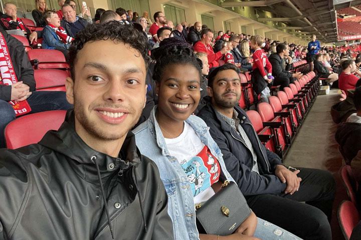 A group of three people sitting together and smiling at the camera at a football match