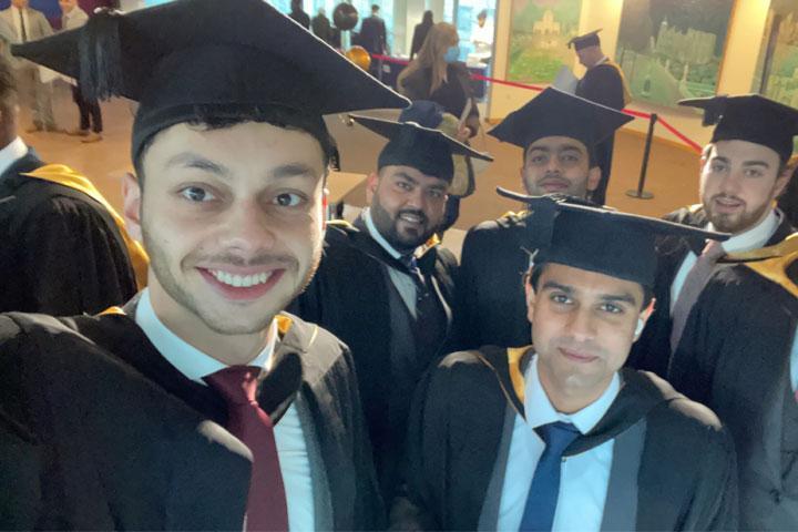 A group of smiling students looking at the camera, wearing graduation caps and gowns.