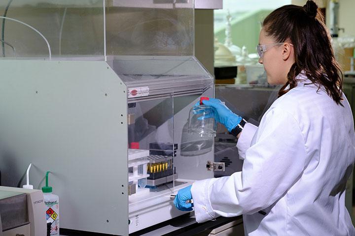 A person wearing protective lab clothing, using peptide synthesizer equipment in a lab.