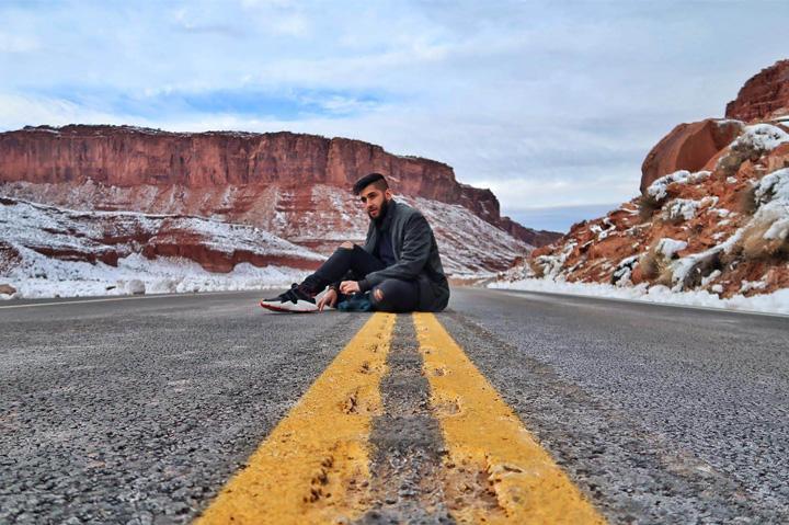 A shot of student Zeeshan Javed sat on a road in the middle of the mountains