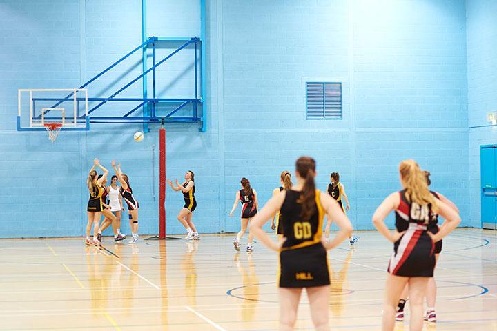 Female students playing netball in the sports hall