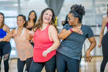Two ladies laughing whilst dancing in a fitness class