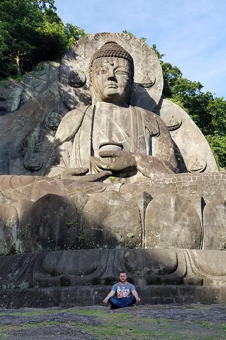 University of Bradford student Xander sitting in front of a large Buddha statue