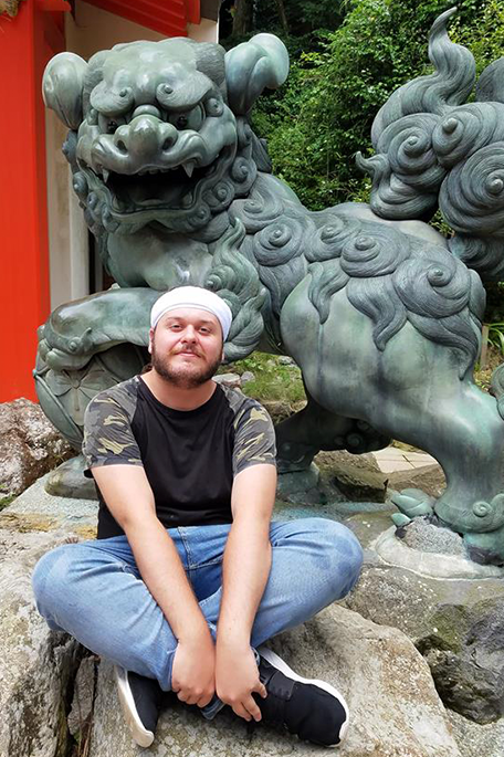 University of Bradford student Xander sitting in front of a jade dragon statue