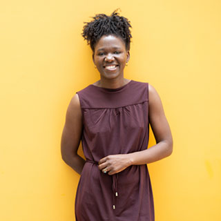 A person standing against a plain yellow wall, smiling at the camera.