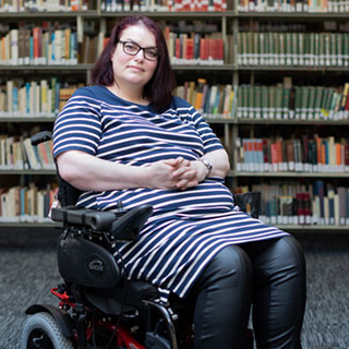 A person in a library facing the camera, with a shelf of library books in the background.