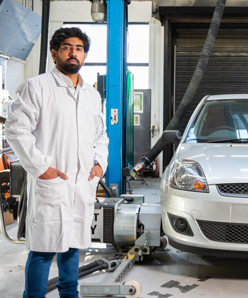 A student in an automotive workshop standing beside a car