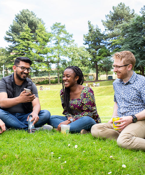 Four students sat on grass, laughing together on a sunny day.