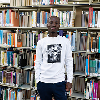 A student standing in front of a full bookcase smiling at the camera