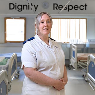 Student stood in nurses uniform in front of a sign that reads "Dignity, Respect"